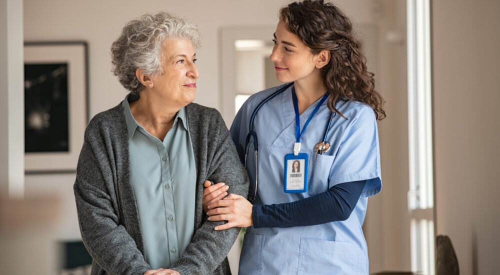 Young caregiver helping senior woman walking. Nurse assisting her old woman patient at nursing home. Senior woman with walking stick being helped by nurse at home.