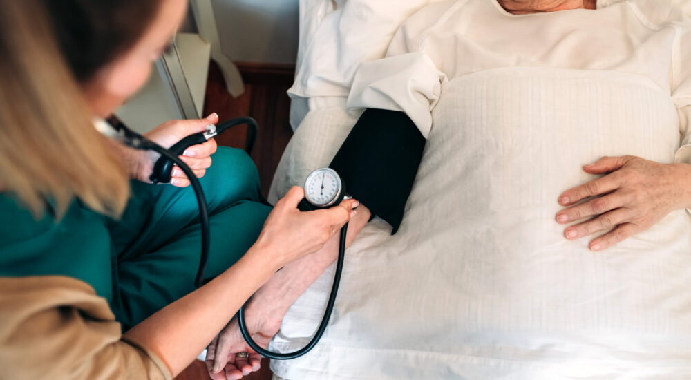 Unrecognizable female caregiver checking blood pressure to a senior woman at home