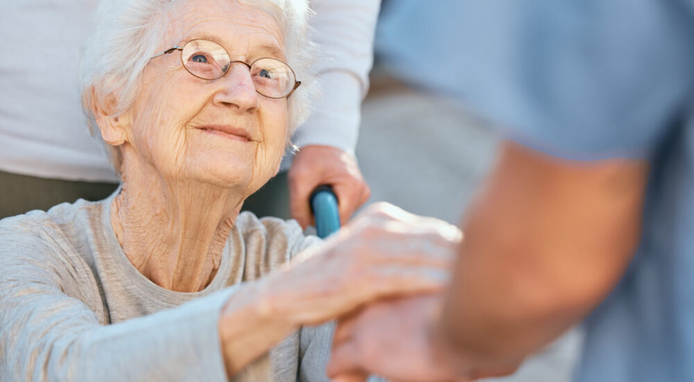 Holding hands, caregiver and senior woman in wheelchair for support outdoor in retirement home. Lov.